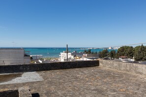 A coastal view from a rooftop terrace with a clear sky, a sea view, and buildings in the background.