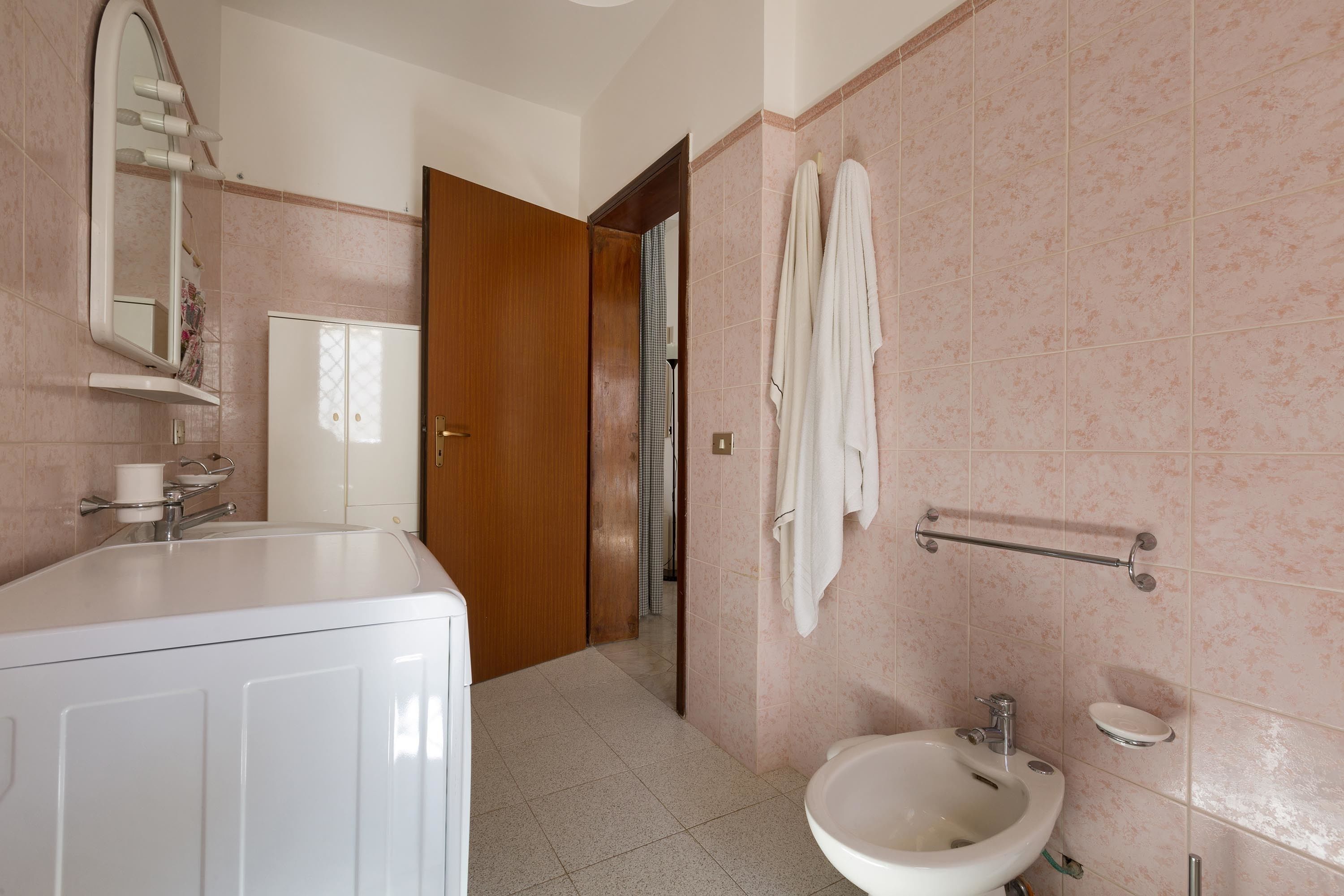 Une salle de bain équipée d’un lavabo, d’un miroir, d’un porte-serviettes et d’une porte donnant sur une autre pièce.