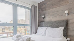 Ett modernt hotellrum med en stor säng, en sänggavel i trä och utsikt över staden genom stora fönster.