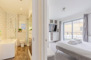 A modern bathroom with a bathtub, toilet, and shower. The room has a large window and a balcony with a view. - Bright 2 Bedroom Flat in Lambeth With Balcony (London)