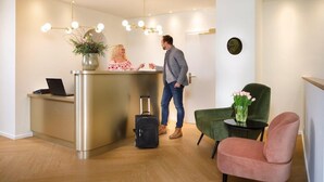 Ett receptionsområde med ett skrivbord, en bärbar dator, en grön stol, en rosa stol och en växt.