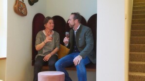 Två personer sitter på en bänk i ett rum med en trappa och en vägghängd väska.