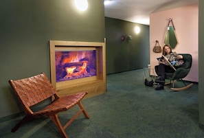 A room with a fireplace, a rocking chair, and a chair with a woven backrest.