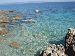 A coastal scene with clear turquoise water, rocky formations, and a distant view of the sea. - Hotel Carmen (Marcana)