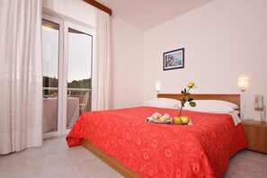 A hotel room with a bed, a table with a tray of food, a vase with flowers, and a painting on the wall. - Hotel Carmen (Marcana)