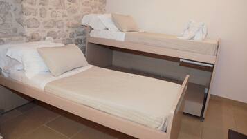 Ein Stockbett mit einem unterem Bett und einem Einzelbett, beide mit weißen Bettwäsche und Kissen.