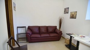 Una sala de estar con un sofá de cuero marrón, una silla de madera, una mesita con una cesta y dos cuadros en la pared.