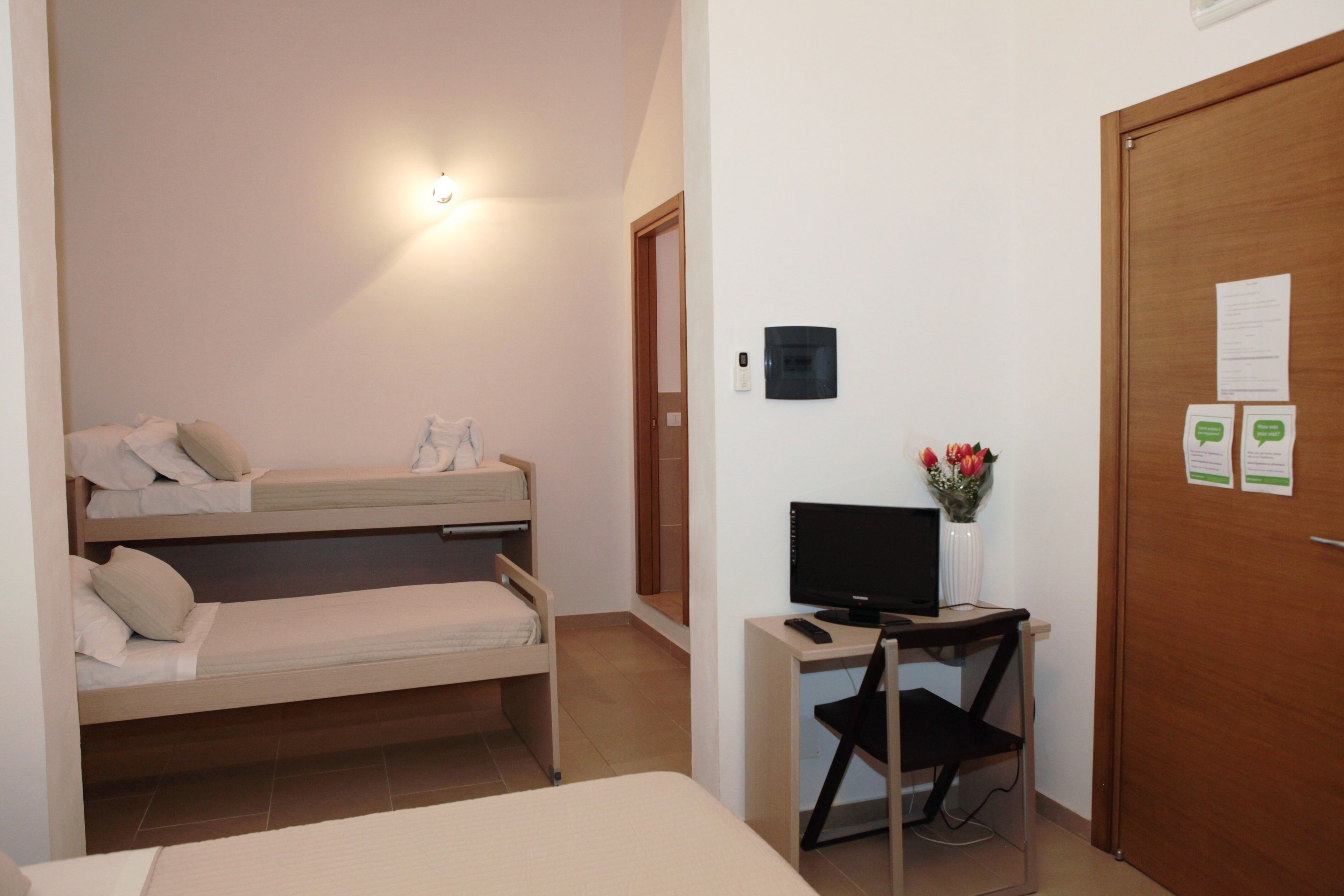 Una habitación con literas, un escritorio con computadora y una puerta con un tablón de anuncios.