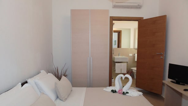 Un dormitorio con cama, armario, televisor y baño visible a través de una puerta abierta.