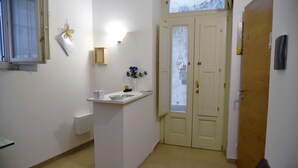 Un pasillo con mostrador de recepción blanco, una lámpara fijada a la pared, una puerta con paneles de vidrio esmerilado y una ventana con vistas a árboles.