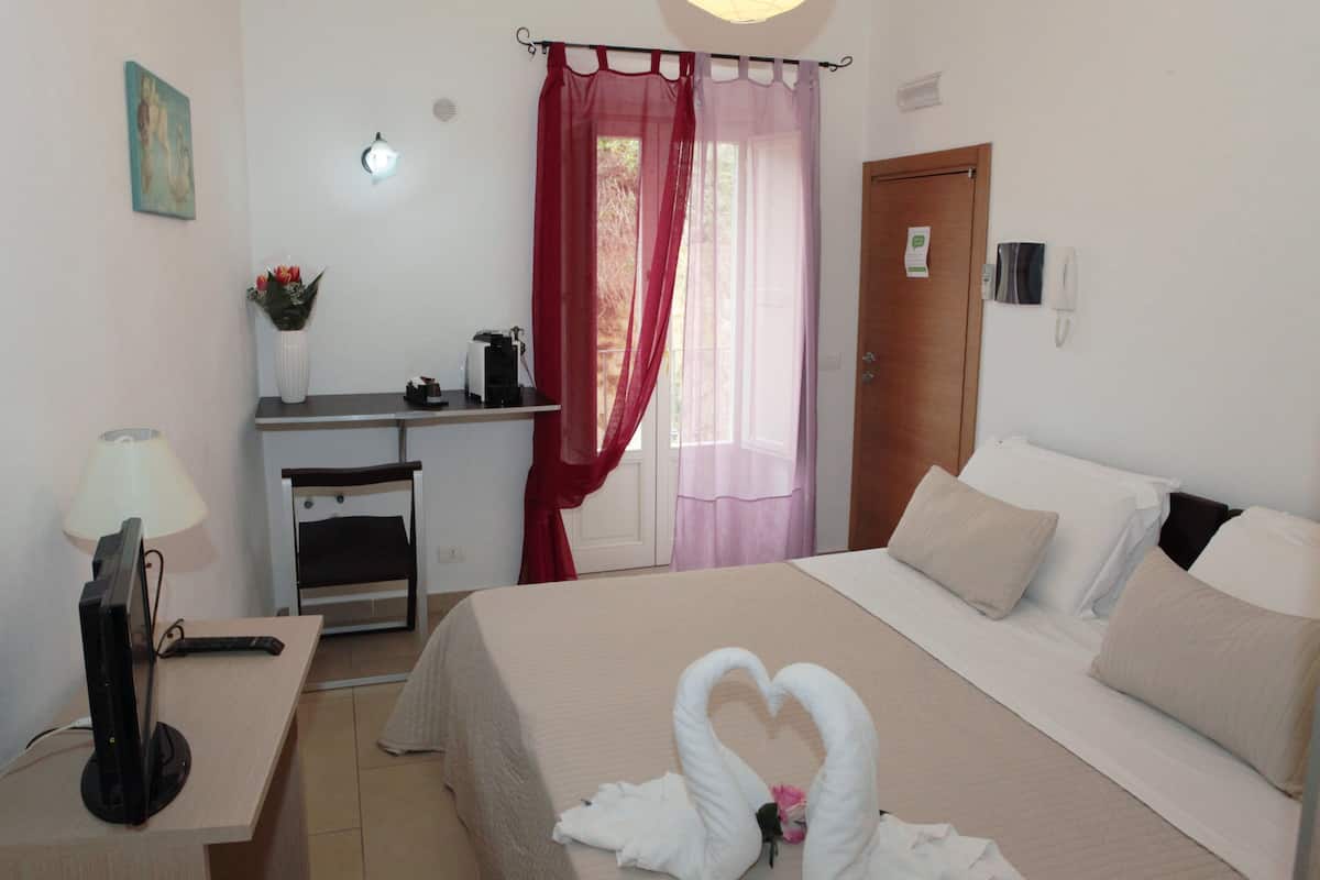 Une chambre d’hôtel avec un lit, un bureau avec un ordinateur, une lampe et un vase rempli de fleurs.