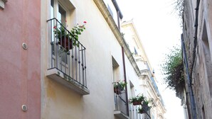 Una estrecha calle adoquinada bordeada por edificios con balcones, algunos con plantas en macetas.