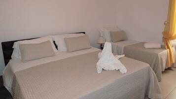 Habitación de hotel con dos camas, cada una con colcha y almohadas color beige. Entre las camas, una mesita de noche con una lámpara.