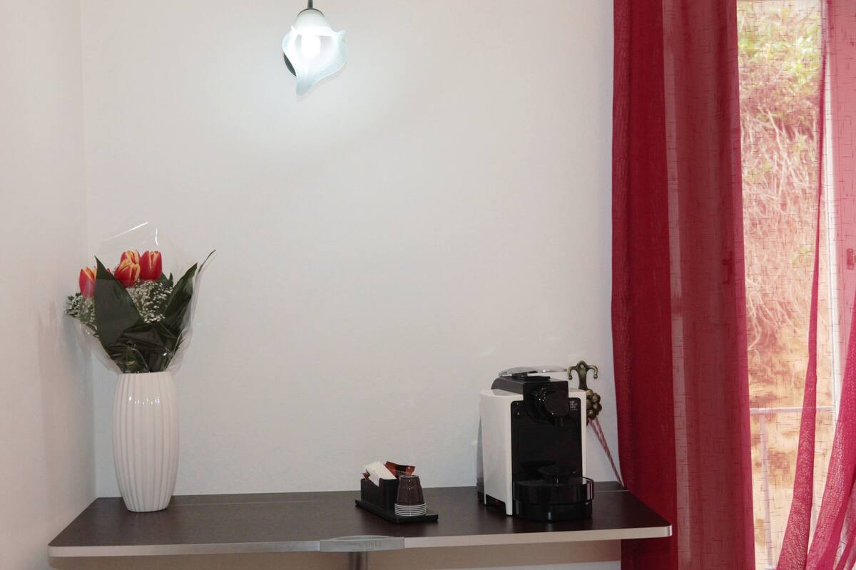 Une pièce avec un vase blanc rempli de fleurs, une machine à café et une petite table.