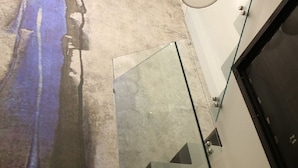 Una escalera moderna con barandillas de vidrio y una pared de concreto con un cuadro abstracto azul.