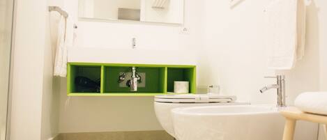 Un baño con inodoro, bidé y un estante verde debajo del espejo.
