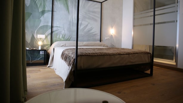 Un dormitorio moderno con cama, mesita de noche, luz empotrada en la pared y un ventanal grande.