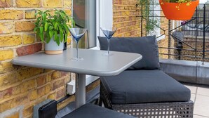 Ein Balkon mit Ziegelwand, einem Tisch mit Topfpflanze, einer hängenden Pflanzschale mit Blumen und Gartenmöbeln.