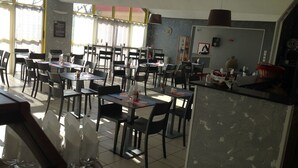 Un comedor con varias mesas y sillas, una encimera de cocina y un reloj en la pared.