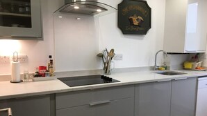 A modern kitchen with a white countertop, grey cabinets, a black induction cooktop, and a stainless steel sink. - Bright, Spacious 2 Bedroom Apartment in Stockbridge (Edinburgh)