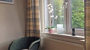 A room with a wicker chair, a radiator, a window with a view of trees, and a potted plant on the windowsill. - Bright, Spacious 2 Bedroom Apartment in Stockbridge (Edinburgh)