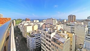 A cityscape with multiple high-rise buildings, a clear blue sky, and a distant view of the sea. - MZapartments Raul Penthouse 03 (Rio de Janeiro)