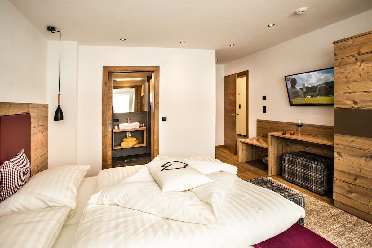 Ein Schlafzimmer mit einem Bett, einem Holz-Kopfbrett, einem Nachttisch, einem Spiegel, einem an der Wand befestigten Fernseher und einem Holzschrank.