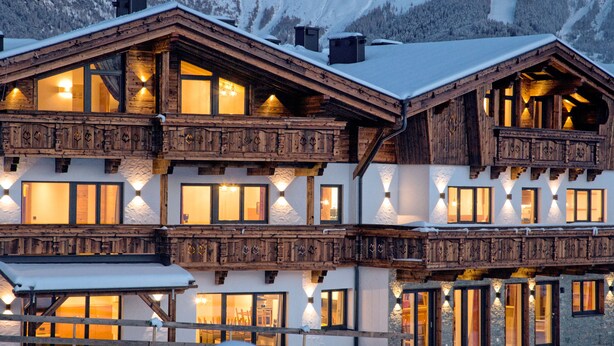 A multi-story wooden chalet with balconies and large windows, surrounded by snow. - Alpinium (Fiss)