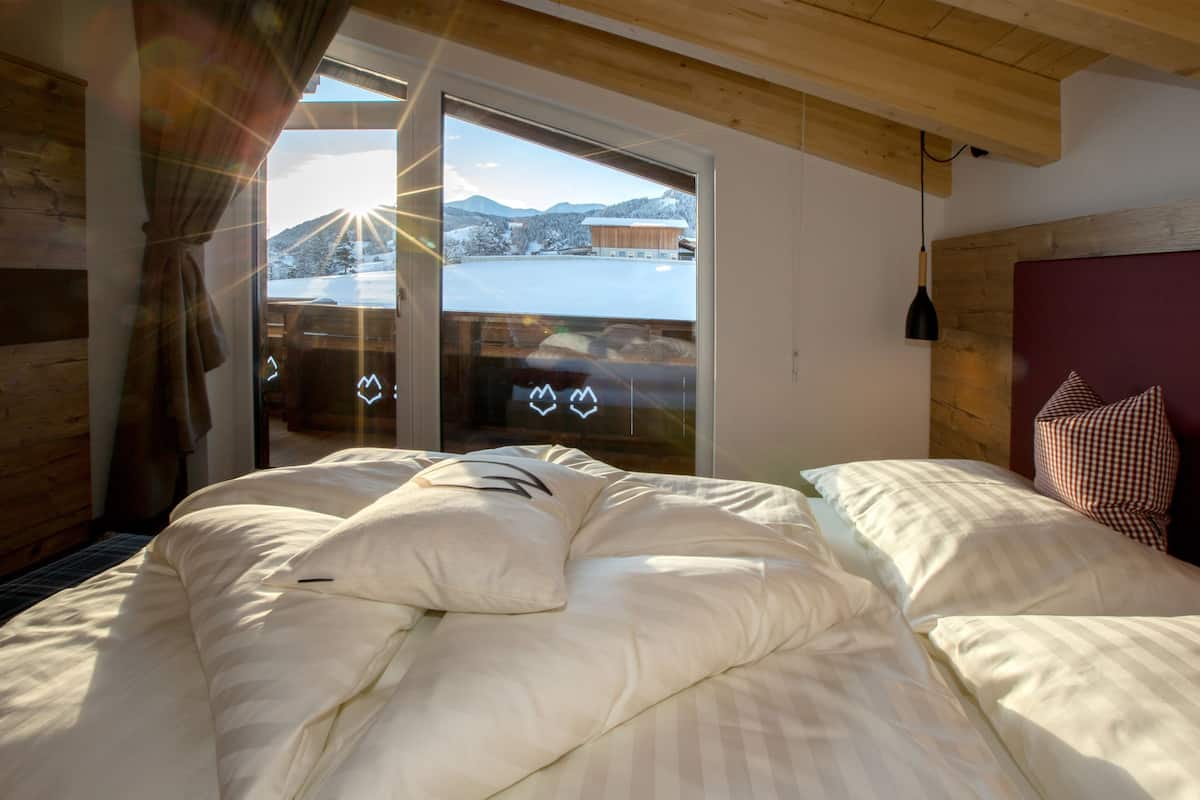 Ein Schlafzimmer mit einem großen Bett, Holzboden und Blick auf eine verschneite Landschaft durch eine Glastür.
