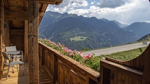 A wooden balcony with a view of a mountain range and a road. - Alpinium (Fiss)