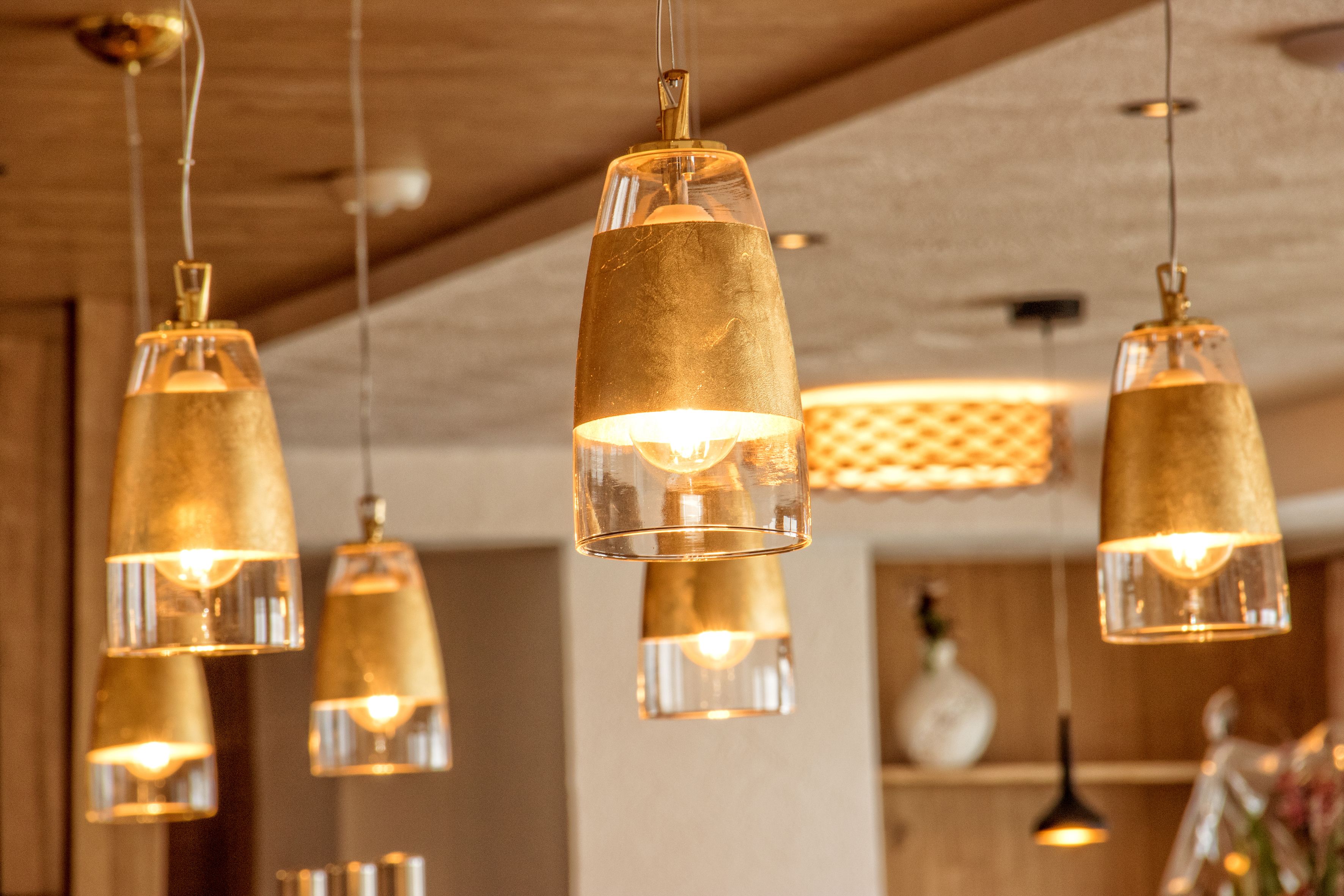 Mehrere Pendelleuchten mit klarer Glaskugel und goldfarbenem Fuß, die von einer Decke mit Holzoptik hängen.