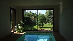 An indoor swimming pool with a view of a garden and trees through large glass doors. - Jardins en Ville (Cognac)