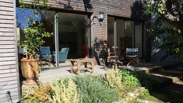 A modern house with a patio area featuring outdoor furniture and a large planter. - Jardins en Ville (Cognac)