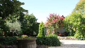 A garden with a large planter, a gravel path, and a stone wall. - Jardins en Ville (Cognac)