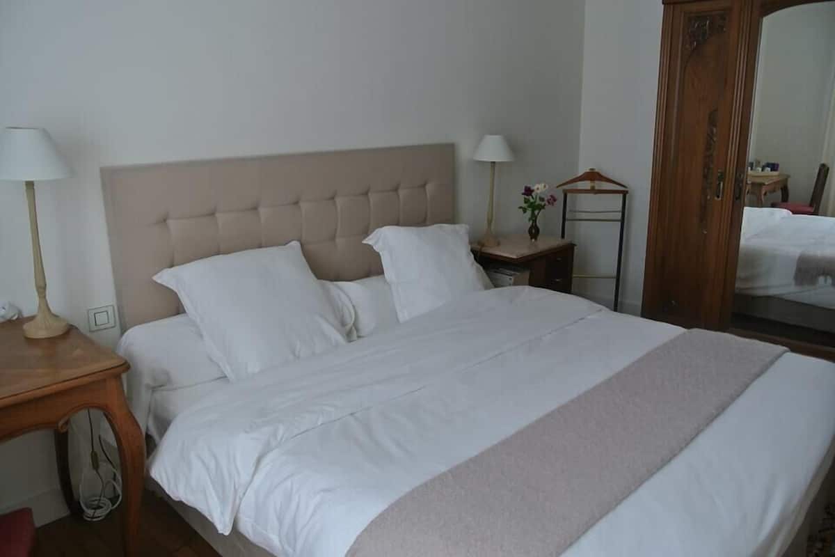 Een keurig opgemaakt bed met een gestuufd hoofdbord, een nachtkastje met een lamp, en een spiegel aan de muur.