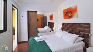 A hotel room with a large bed, a green bedspread, white bedding, a wooden headboard, a painting on the wall, and a mirror reflecting the room.