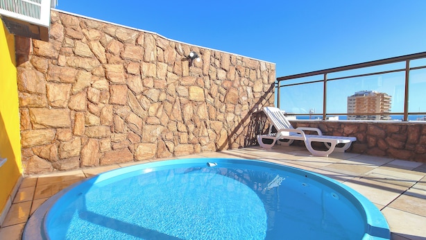 A rooftop pool with stone walls and a clear blue sky.