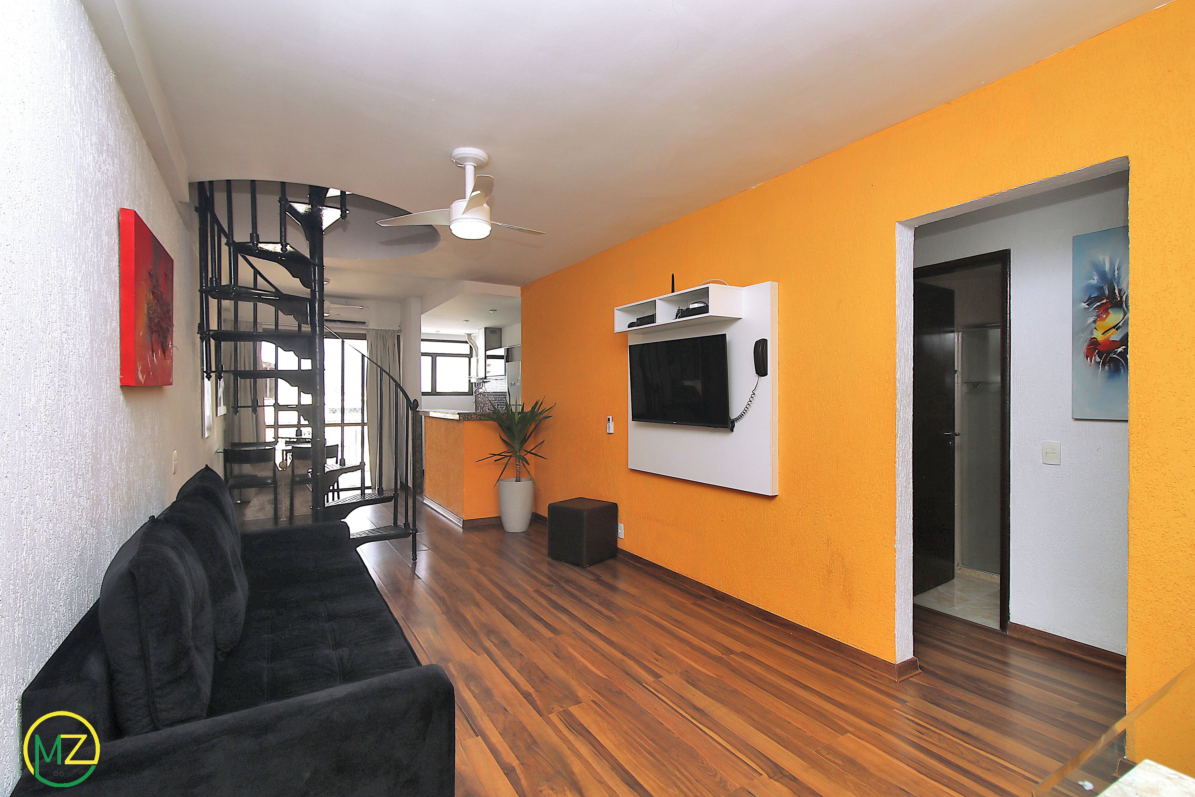 A modern living room with a black sofa, wooden flooring, a ceiling fan, and a staircase leading to another level.