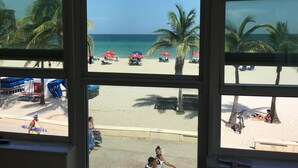 Vista de una playa con palmeras, sombrillas y sillas de playa a través de una ventana.