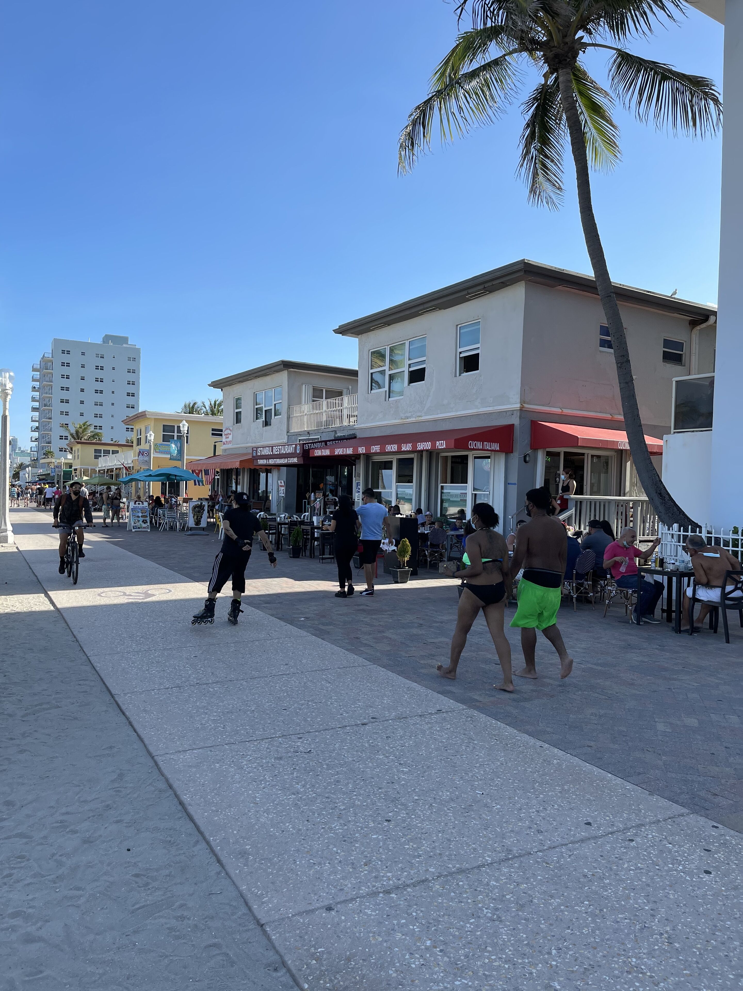 A bustling street scene with outdoor seating at a restaurant, a cyclist, and pedestrians.