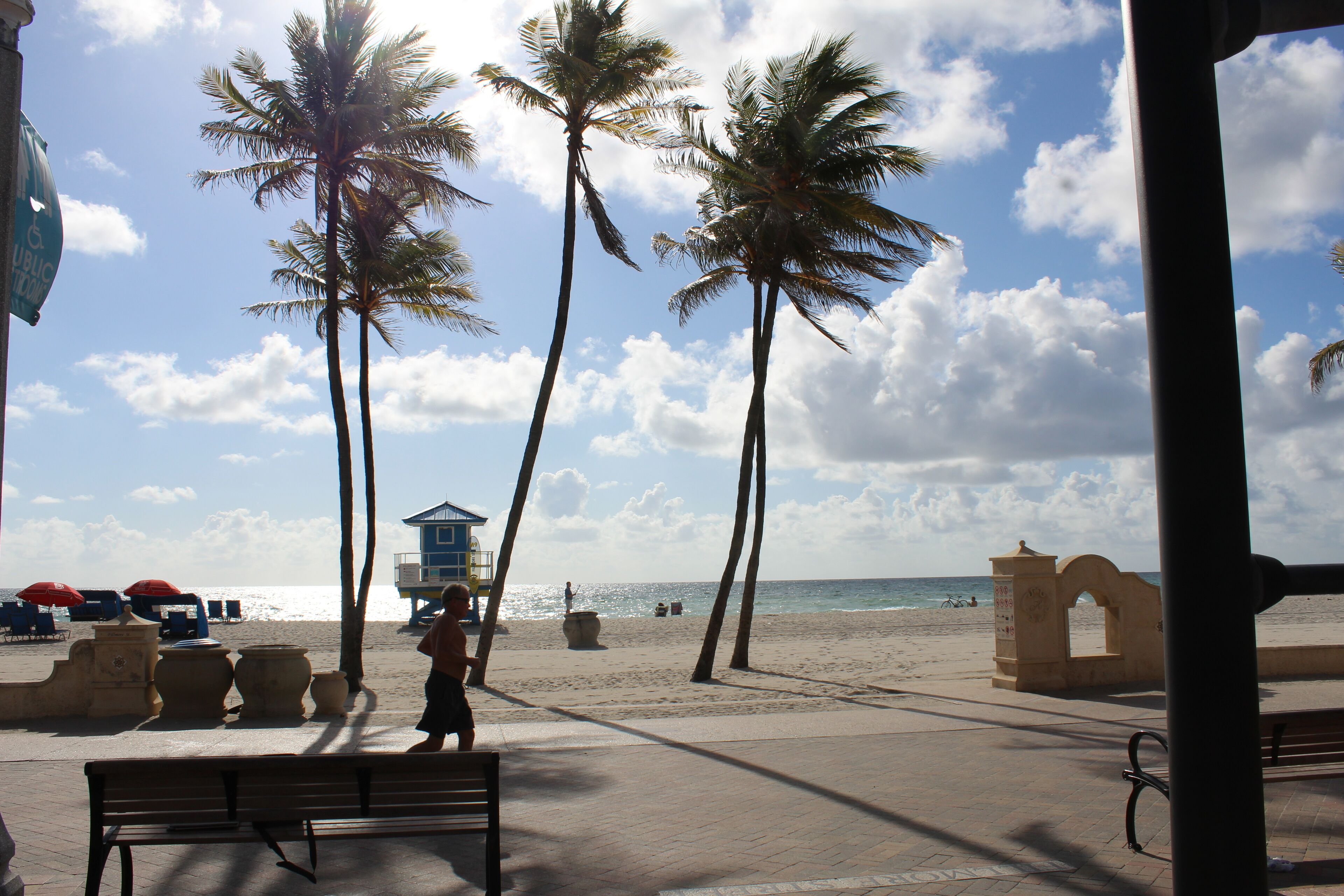 Un paseo marítimo en la playa con palmeras, una torre de salvavidas y un banco.