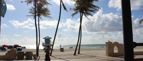 Un paseo marítimo en la playa con palmeras, una torre de salvavidas y un banco.