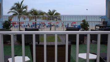 A balcony with outdoor furniture, a view of the beach, and palm trees.