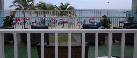 A balcony with outdoor furniture, a view of the beach, and palm trees.