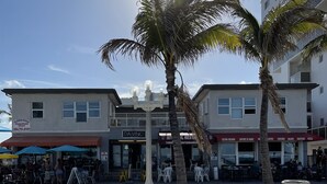 Zona frente al mar con palmeras, una playa arenosa y edificios con tiendas y restaurantes.
