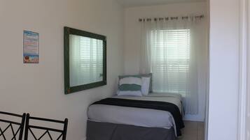 Un dormitorio con cama, espejo, ventana con persianas y puerta.