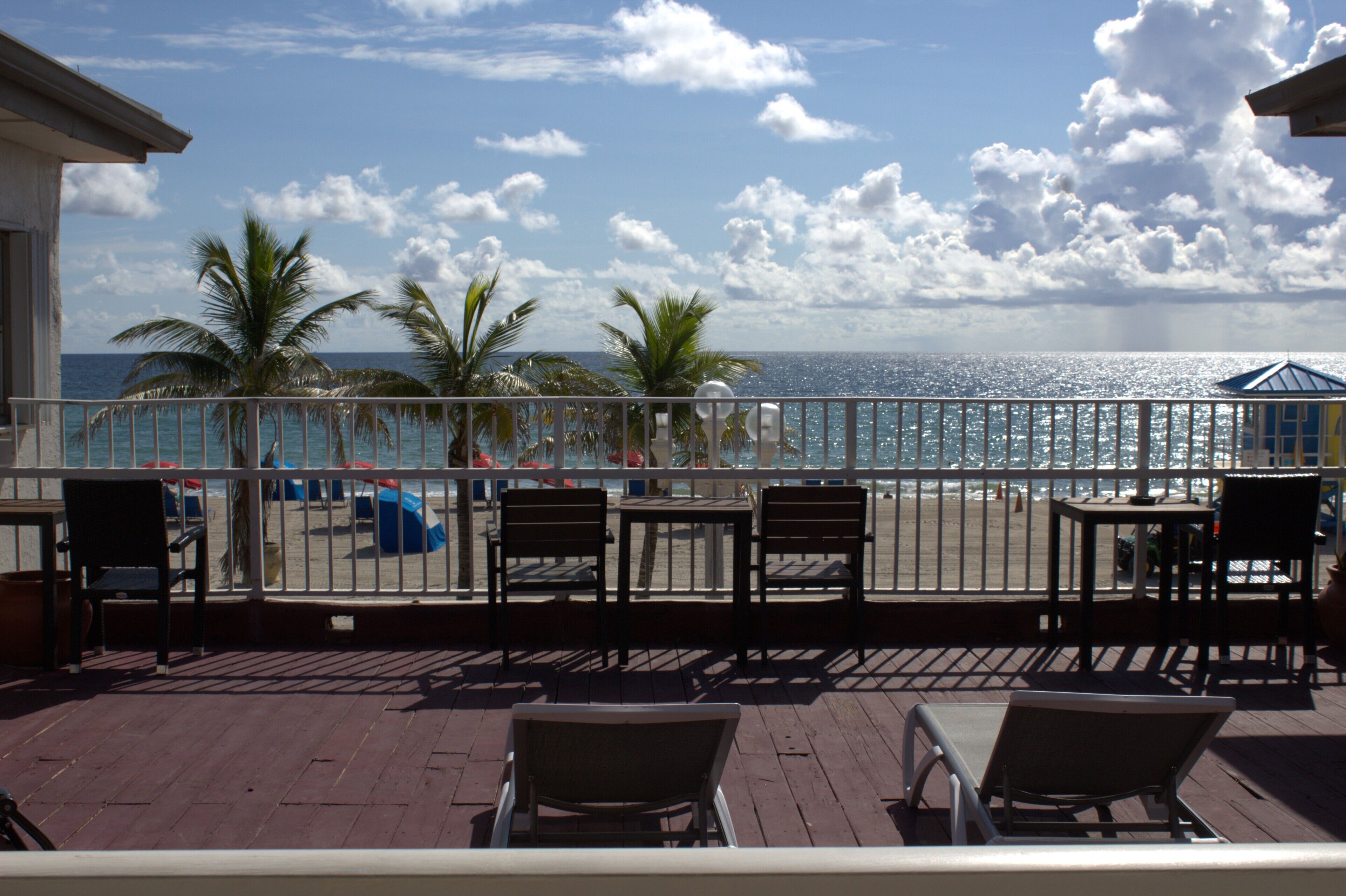 Eine Terrasse mit Stühlen und Tischen, mit Blick auf einen Strand mit Palmen und dem Meer.