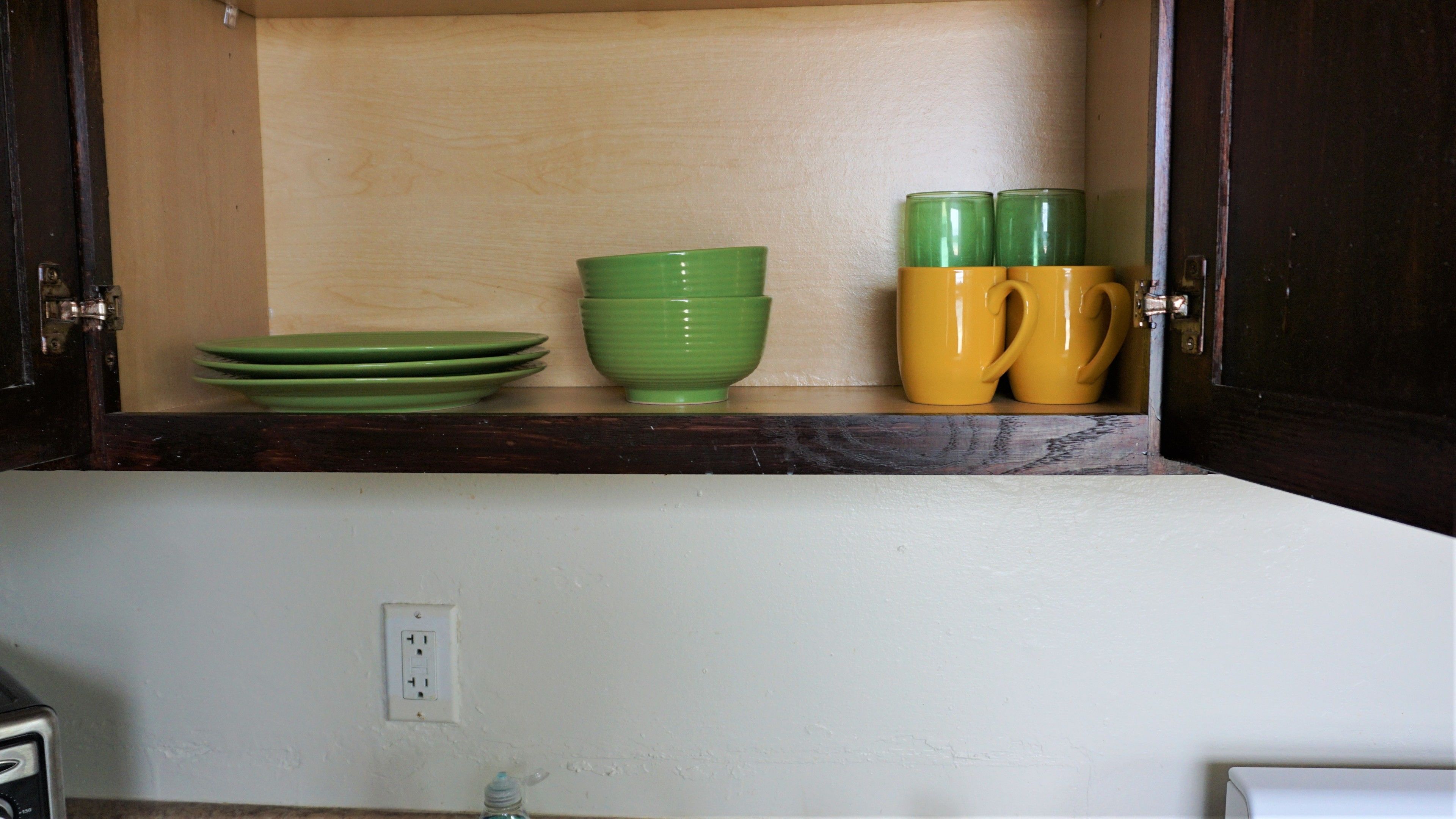 A kitchen cabinet with green and yellow dishes and a single green bowl.
