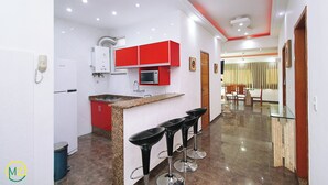 A modern kitchen with red cabinets, a built-in microwave, and a granite countertop. There are three black bar stools with chrome bases. The kitchen leads to a dining area with a wooden table and chairs. - MZapartments Nossa Senhora Penthouse (Rio de Janeiro)