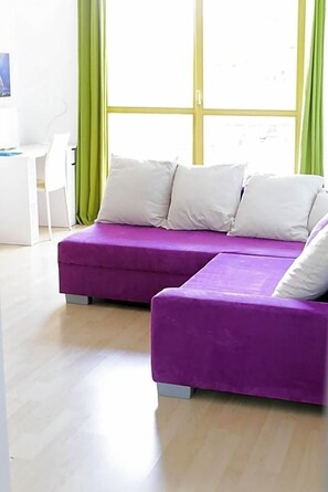 A modern room with a purple sofa set, a white chair, and a large window with green curtains.